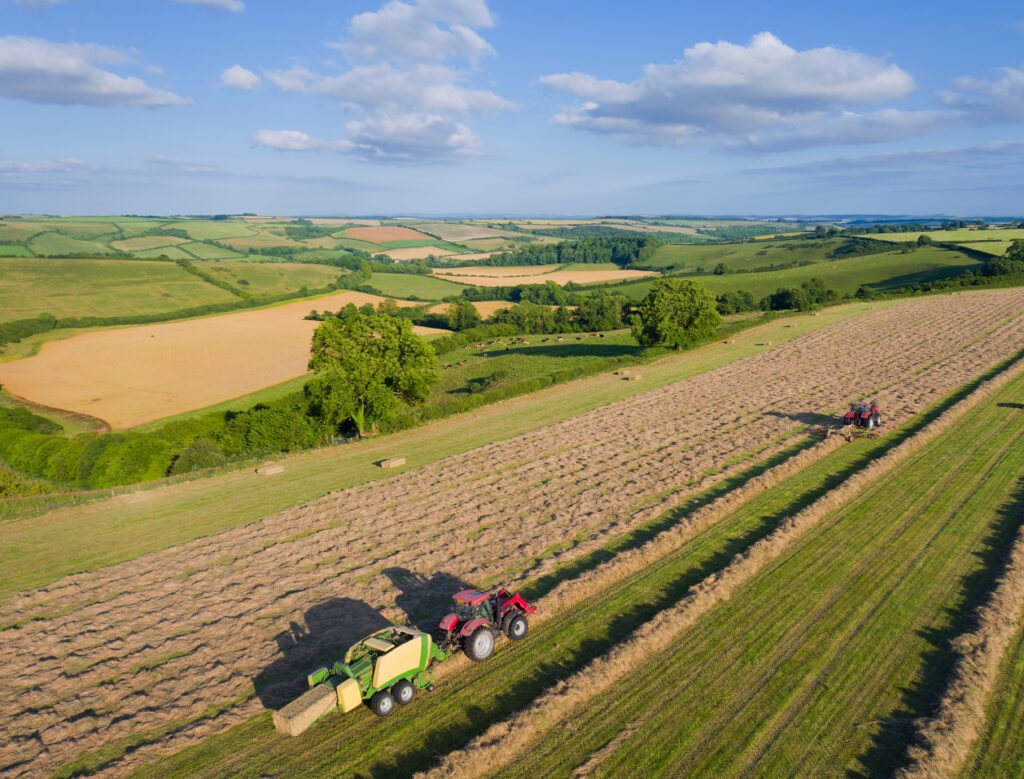 Vista aérea de tractores empacando heno en campo agrícola con paisaje rural